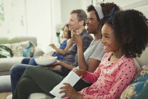 Aufpassender Film der jungen multiethnischen Familie und Essen des Popcorns auf Sofa