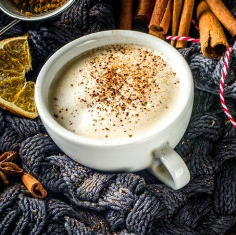 süßes heißes Getränk des Herbstes, Rum mit Chai-Butter, Kürbiskuchen oder Kürbisgewürzkaffee Latte gemütlicher Herbsthintergrund mit traditioneller Latte-Tasse, Gewürzen und altem Pullover, auf rustikalem hölzernem Hintergrund