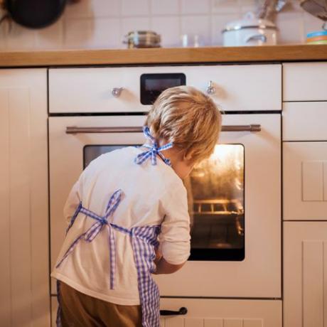 Kleiner Junge, der in den Ofen drinnen schaut und backt