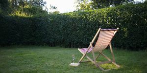 Ein einzelner Liegestuhl mit einem Buch und Sekt in einem ländlichen Garten.