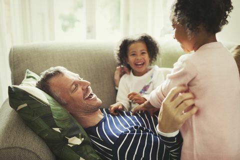 Vater und Töchter kitzeln und lachen auf dem Sofa