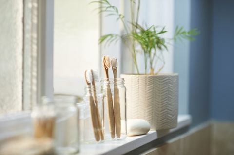 plastikfreie Holz-Familienzahnbürsten in einem Glasgefäß neben anderen Zero-Waste-Produkten auf einem Badezimmerfensterbrett
