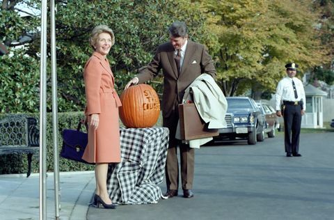 auf diesem foto bewundert präsident ronald reagan einen kürbis, in den der slogan " bleib den kurs" eingraviert ist. präsident reagan verwendete den slogan während der 1982 Zwischenwahlen First Lady Nancy Reagan posiert neben dem Kürbis Die beiden stehen vor dem südlichen Portikuseingang zum Weißen Haus