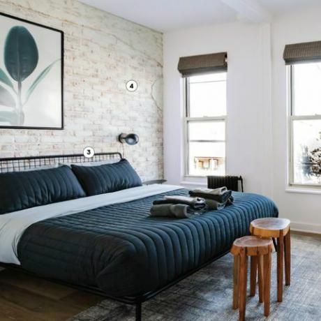 Schlafzimmer mit weiß getünchten Ziegeln, schwarzem Drahtrahmenbett mit blauer Bettdecke