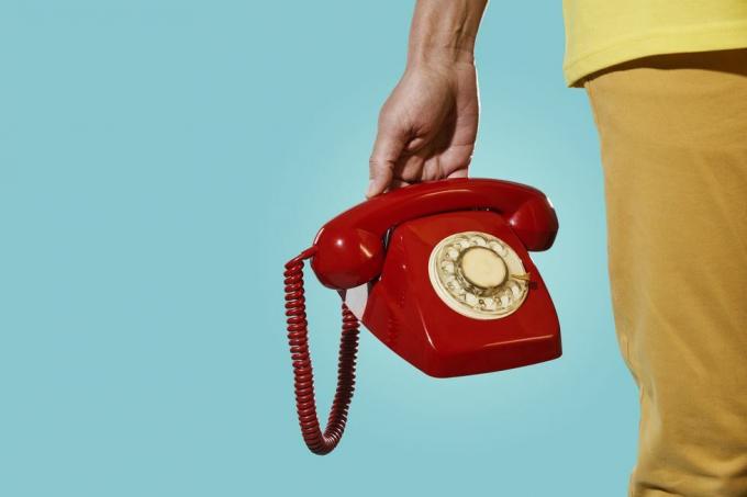 Mann mit einem alten roten Telefon in der Hand