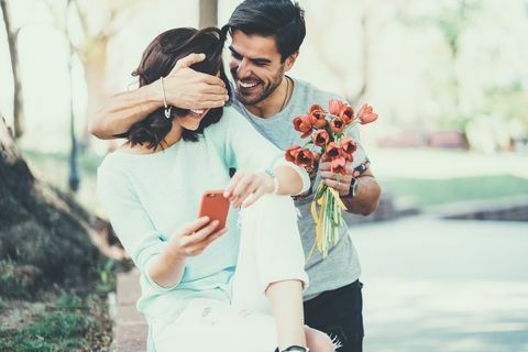 Junger Mann, der seine Freundin mit Blumenstrauß von Tulpen überrascht