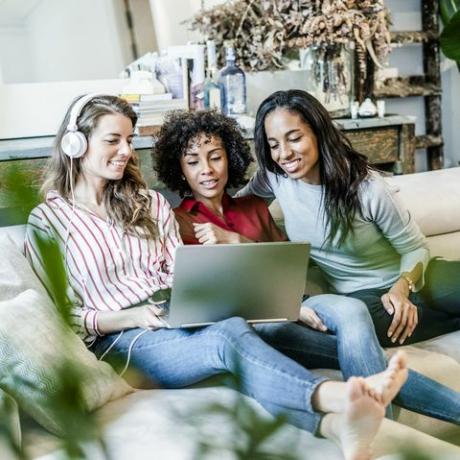 Drei glückliche Frauen mit Laptop sitzen auf der Couch