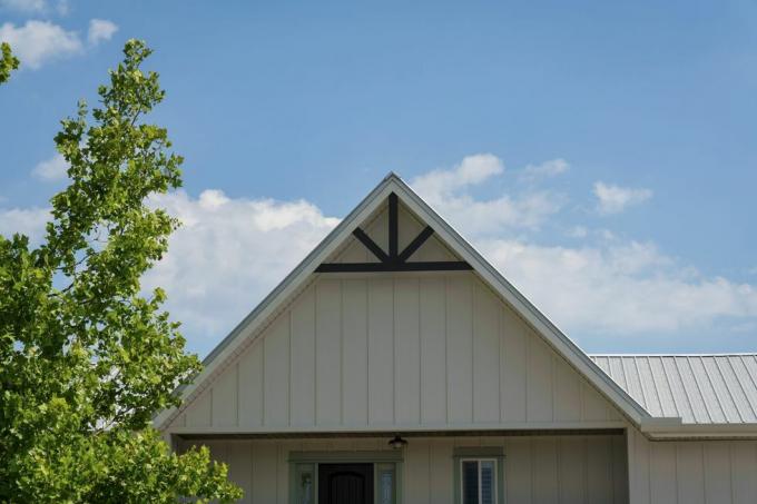 Destin, Florida Cottage-Dachspitze mit weißem Brett und Lattenverkleidung und schwarzen Verzierungen. An der Vorderseite des Cottages steht ein Baum mit einem Himmelshintergrund