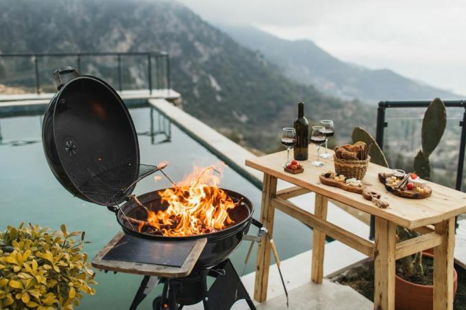 Vorbereitung auf eine luxuriöse Grillparty im Freien, brennendes Feuer im Grill, Tisch mit Snacks und Wein