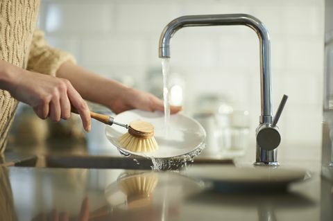 Eine Frau verwendet eine plastikfreie Bürste, um Geschirr in einer Küchenspüle zu reinigen, Nahaufnahme