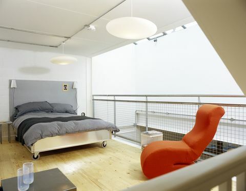 Modernes Schlafzimmer mit grauem Bettbezug und hellem orange Stuhl