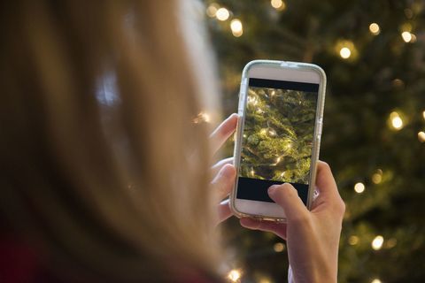 Frau, die Weihnachtsbaum mit Handy fotografiert