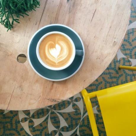 Tasse Kaffee mit Herzschaum im aquamarinen Becher auf Holztisch