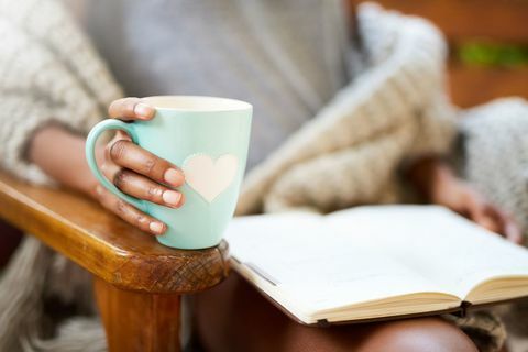 Geernteter Schuss einer Frau, die mit einem Buch und einem Tasse Kaffee sich entspannt