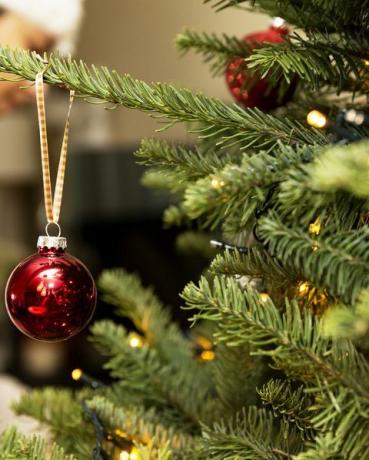 Defokussierte Frau, die an hängenden Ornamenten an einem Baum arbeitet, mit einer Nahaufnahme eines Baumschmucks, der an der Seite hängt