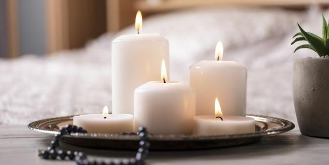 Komposition aus weißen brennenden Kerzen auf dem Nachttisch im hellen, gemütlichen Schlafzimmer-Interieur mit selektivem Fokus