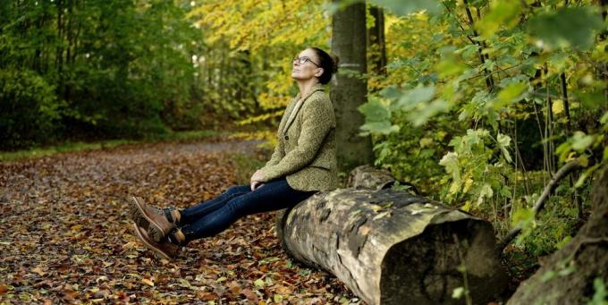 Reife Frau sitzt auf einem Baumstamm in einem herbstlichen Wald