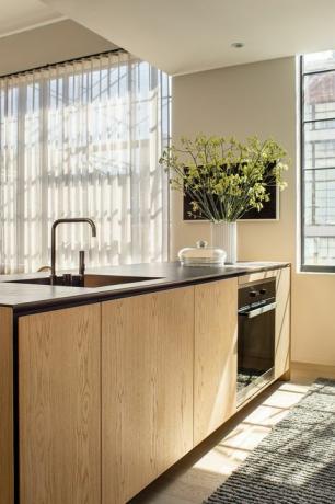 Kücheninsel aus Holz, schwarze Arbeitsplatten, Wollläufer, weiße Vase, Wasserhahn